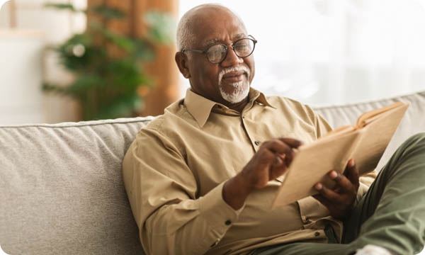 Senior Man Reading Book Sitting on Couch at Home